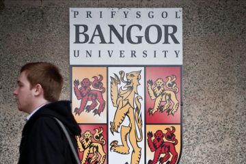 Student walking by Bangor University crest shield logo Student walking by Bangor University crest shield logo