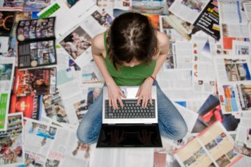 A woman types on her laptop on a carpet of newspapers, symbolising student journalism