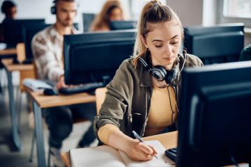 A university student writes notes while e-learning on a computer in the classroom