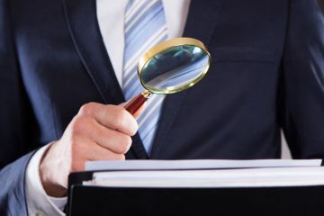 Suited businessman examining paperwork with magnifying glass Suited businessman examining paperwork with magnifying glass