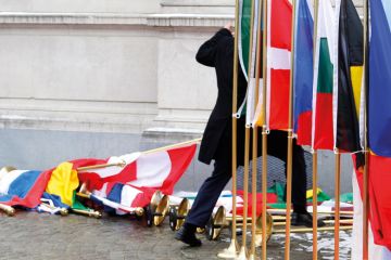 Suited man setting up row of international flags Suited man setting up row of international flags