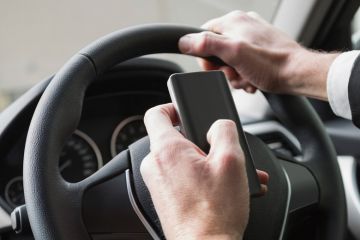 Suited man typing on phone while driving