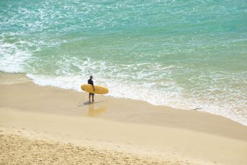 Surfer stands at waters edge hold surfboard waiting to enter Surfer stands at waters edge hold surfboard waiting to enter