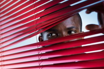Suspicious man looking through venetian blinds