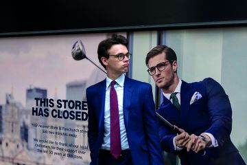 A businessman pauses next to a closed shop poster featuring a similar man also wearing a blue suit and enjoying leisure time on the golf course A businessman pauses next to a closed shop poster featuring a similar man also wearing a blue suit and enjoying leisure time on the golf course