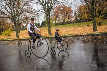 child rides past adult on high-wheel bicycles