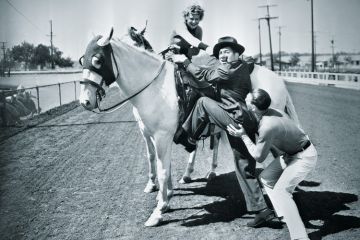 Young couple trying to help a man get onto his horse Young couple trying to help a man get onto his horse