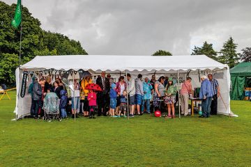 People standing under larger tent to shelter from rain