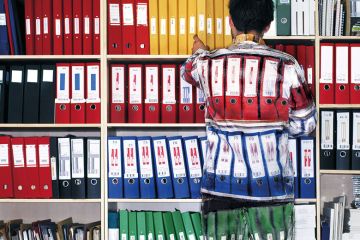 Man wearing camouflage suit matching shelves of folders Man wearing camouflage suit matching shelves of folders