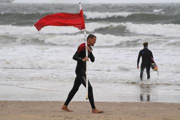 Image of man walking on beach holding red flag Image of man walking on beach holding red flag
