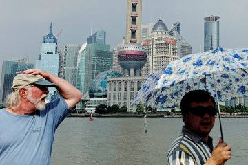 People walk along the Bund in front of the skyline of the city's financial district of Pudong, in Shanghai