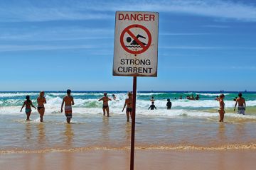 People in the sea at Manly beach, Australia with "dangerous currents" sign. People in the sea at Manly beach, Australia with "dangerous currents" sign.
