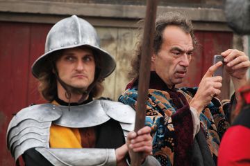 Background actor takes a picture using a smart phone next to another background actor dressed as a medieval guard