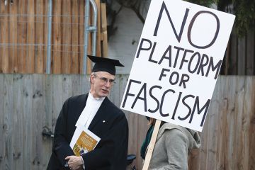 A proctor speaks to a protester holding a "No platform for fascism" placard