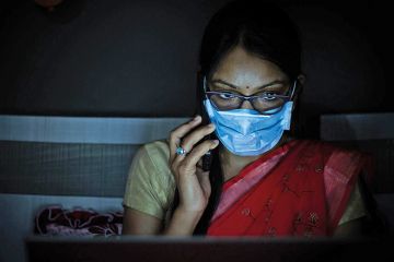 Young Indian Woman wearing mask working on her laptop and talking on phone Young Indian Woman wearing mask working on her laptop and talking on phone