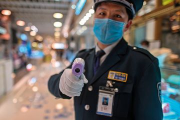 A guard wearing a facemask amid concerns over the spread of the COVID-19 novel coronavirus, holds a thermal gun to check the body temperature of visitors at the entrance of a restaurant area in Shanghai, on March 21, 2020. A guard wearing a facemask amid concerns over the spread of the COVID-19 novel coronavirus, holds a thermal gun to check the body temperature of visitors at the entrance of a restaurant area in Shanghai, on March 21, 2020.