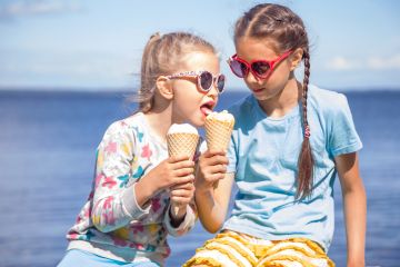 Two girls wearing eating ice cream on the seashore