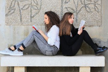 Two students sitting back to back reading books
