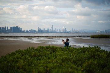 A man takes a photo from the shoreline of Hong Kong’s Deep Bay with the skyline of Chinese mainland city of Shenzhen visible behind him A man takes a photo from the shoreline of Hong Kong’s Deep Bay with the skyline of Chinese mainland city of Shenzhen visible behind him