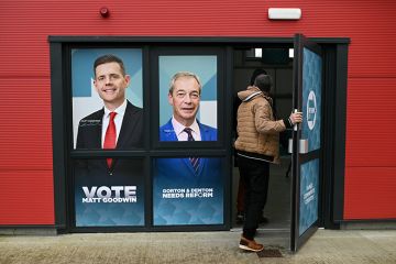 A person walks through a doorway printed with the faces of Reform UK candidate Matt Goodwin and Reform UK leader Nigel Farage during an event ahead of the February 26 Gorton and Denton by-election, in Denton, northwest England on 5 February, 2026. 