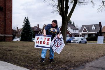 A volunteer places a "Vote Here" sign outside a polling station at McDonald Elementary School in Dearborn, Michigan