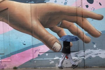 Wall art of hand reaching out with person walking by holding an umbrella in Toronto to illustrate How to meet  students’ soaring mental health  needs on a budget