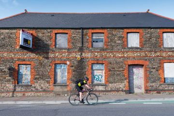 A cyclist rides past a boarded up retail unit to illustrate UK’s university investment zones echo US, but leave questions