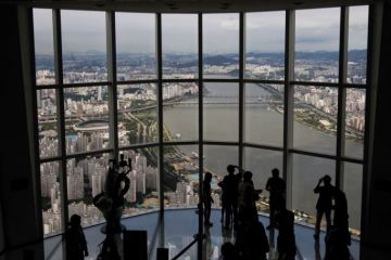 Visitors are silhouetted as they take photographs at the glass-bottomed Seoul Sky observation deck to illustrate UK university explores options in South Korea’s forgotten hub