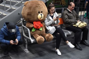 Commuters use their mobile phones next to a giant soft toy bear whilst waiting for a train in Sydney Commuters use their mobile phones next to a giant soft toy bear to illustrate New grant delays hit Australian researchers