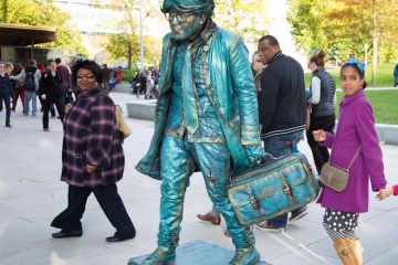 People interact with a living statue artist holing a suitcase to illustrate UK Horizon association ‘dither’ risks ‘more lost science funding’