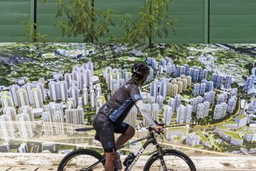 A cyclist rides past an artist illustration of buildings at a construction site in the Kwu Tung area in Hong Kong, China to illustrate ‘University town’ will give Hong Kong campuses room to grow