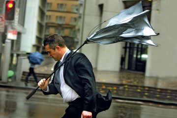 A man's umbrella turns inside-out as he battles strong winds and rain in Sydney to illustrate Rich prosper Down Under