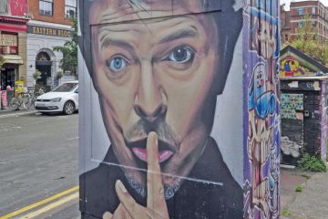 Wall Graffiti of a man with a finger to his lips at the Northern Quarter Art in Stevenson Square Manchester, UK to illustrate Students back employer levy to fund English higher education
