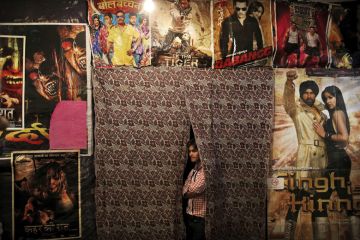 An Indian worker waits for customers as he is surrounded by Bollywood film posters at a small cinema in New Delhi to illustrate India’s JNU target for Bollywood film and ‘jingoistic nationalism’