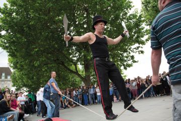 Street performer thrills the crowd with his knife act whilst balancing on a rope slack line being held up by members of the audience Street performer thrills the crowd with his knife act whilst balancing on a rope slack line being held up by members of the audience to illustrate UKRI ‘must regain trust’ of equality committee in Donelan row