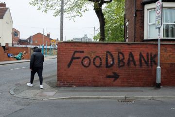 Person passes by bold, black graffiti that points towards a local food bank Person passes by bold, black graffiti that points towards a local food bank to illustrate that One in four UK universities now running a food bank
