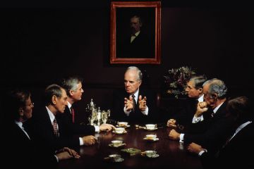 Group of men sitting at a table in a business meeting to illustrate How I learned that keeping men at the top was leaders’ real task