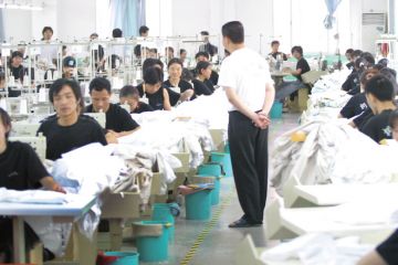 China, sweatshop manager standing watching workers China, sweatshop manager standing watching workers