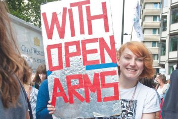 Person in a refugee demonstration London UK holding a banner reading 'With Open Arms' Person in a refugee demonstration London UK holding a banner reading 'With Open Arms'