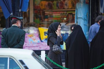 An Iranian woman adjusts her scarf as two veiled morality policewomen talk to them in Tehran to illustrate Iranian scholar who resigned in protest may need to seek asylum