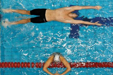 Swimmer in backstroke race with another swimmer standing in the water reading, book, winter