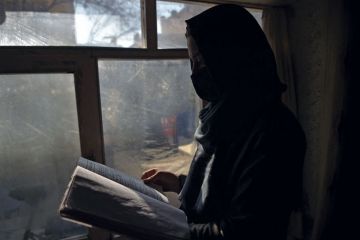Marwa, a student at her home in Kabul reading next to a window as women are now banned from attending university in Taliban