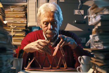 Unproductive senior office worker sitting at desk and building a card castle instead of working