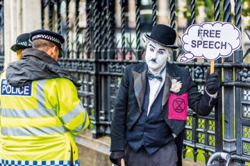 Police question a protester dressed in Chaplin type clothes outside the Houses of Parliament London holding a Free Speech banner. Police question a protester dressed in Chaplin type clothes outside the Houses of Parliament London holding a Free Speech banner to illustrate Labour urged to outline free speech act future as criticism grows