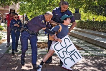 Holding a sign that said Sue USC a USC student is arrested by campus police in USC Village after calling for USC to sued and held accountable for their actions surrounding the pro-Palestinian protest on campus on Monday, May 6, 2024 in Los Angeles, CA 