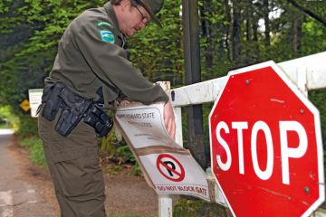 A ranger adjusts stop sign saying the park is closed in Kenmore, WA , Seattle to illustrate US college closures could spread to public universities
