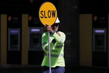 A traffic control worker holds a traffic sign reading "Slow" in Brisbane, Australia A traffic control worker holds a traffic sign reading "Slow" in Brisbane, Australia to illustrate Visa chaos ‘latest driver’ of ‘two-tiered Australian sector’