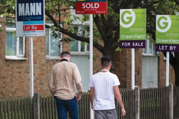 Pedestrians walk past estate agents' 'Let By', 'Sold', and 'For Sale' signs