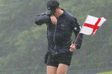 Man  soaking wet as he runs through Wiltshire holding a St Georges Flag.