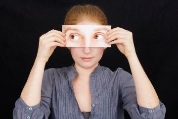 Woman holding print-out of eyes over face Woman holding print-out of eyes over face